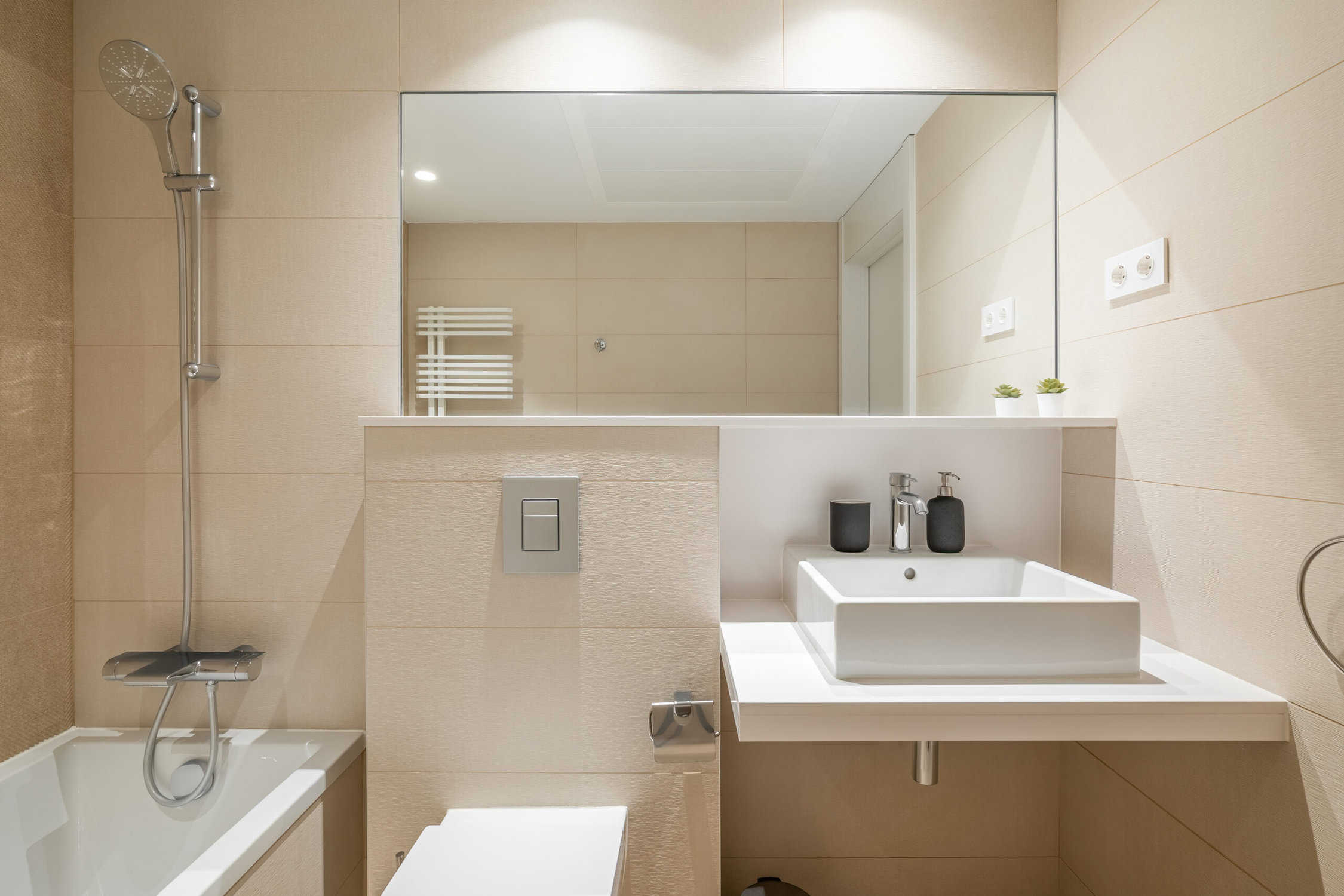 Cozy bathroom in modern design with huge mirror on the wall and bright lighting. Walls are in beige tiles and white sanitary ware- cabinet painters in Erie, CO