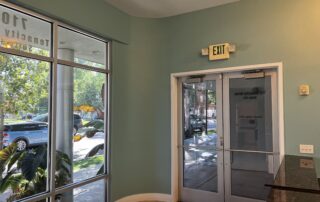 Sage Green Commercial Interior Sage green painted commercial interior with cream trim doorway, exit sign, and glass storefront entrance