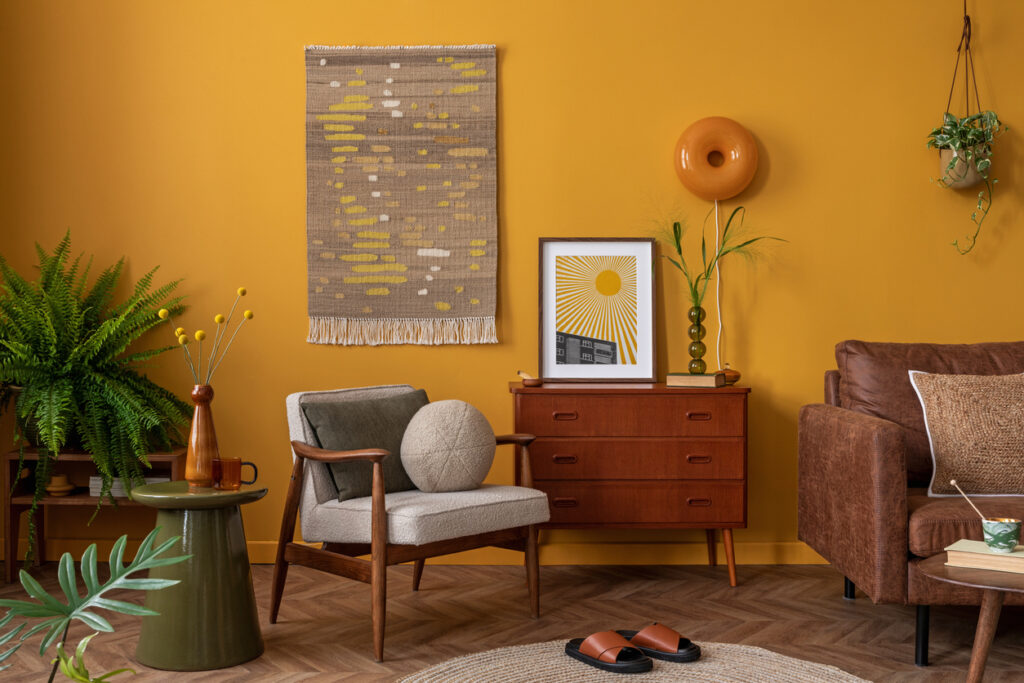 Interior design of warm living room interior with mock up poster frame, stylish kilim rug, wooden sideboard, brown sofa, stylish armchair, green coffee table, yellow wall and personal accessories. Bright living room with neutral walls and large windows