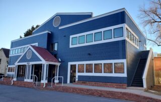 Blue Commercial Building Exterior Navy blue painted commercial building with white-trimmed multi-pane windows, red brick base, and peaked entry vestibule