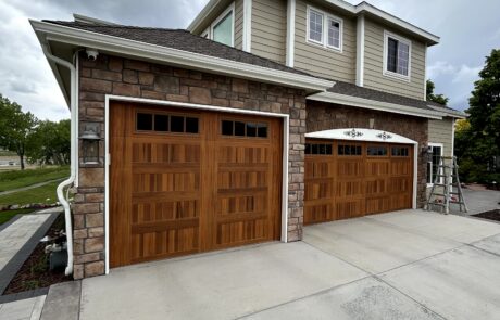 Residential Home Wood Garage Doors Beige residential home with warm wood-tone garage doors, brown stone veneer base, white trim, and concrete driveway