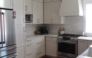 Cream Kitchen Cabinet Refinishing Cream-painted kitchen cabinets with brass hardware, white subway tile backsplash, stainless steel appliances, and white