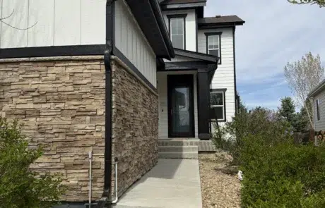 Professional Exterior Painting of Home Entryway and Siding Close up of a home's freshly painted white siding, black trim, stone facade, and dark front door.