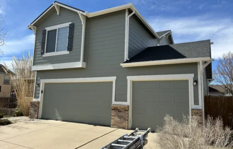 Home exterior painting showcasing new green siding and garage doors Residential home exterior after professional painting, featuring new green siding, crisp white trim, and matching garage doors.