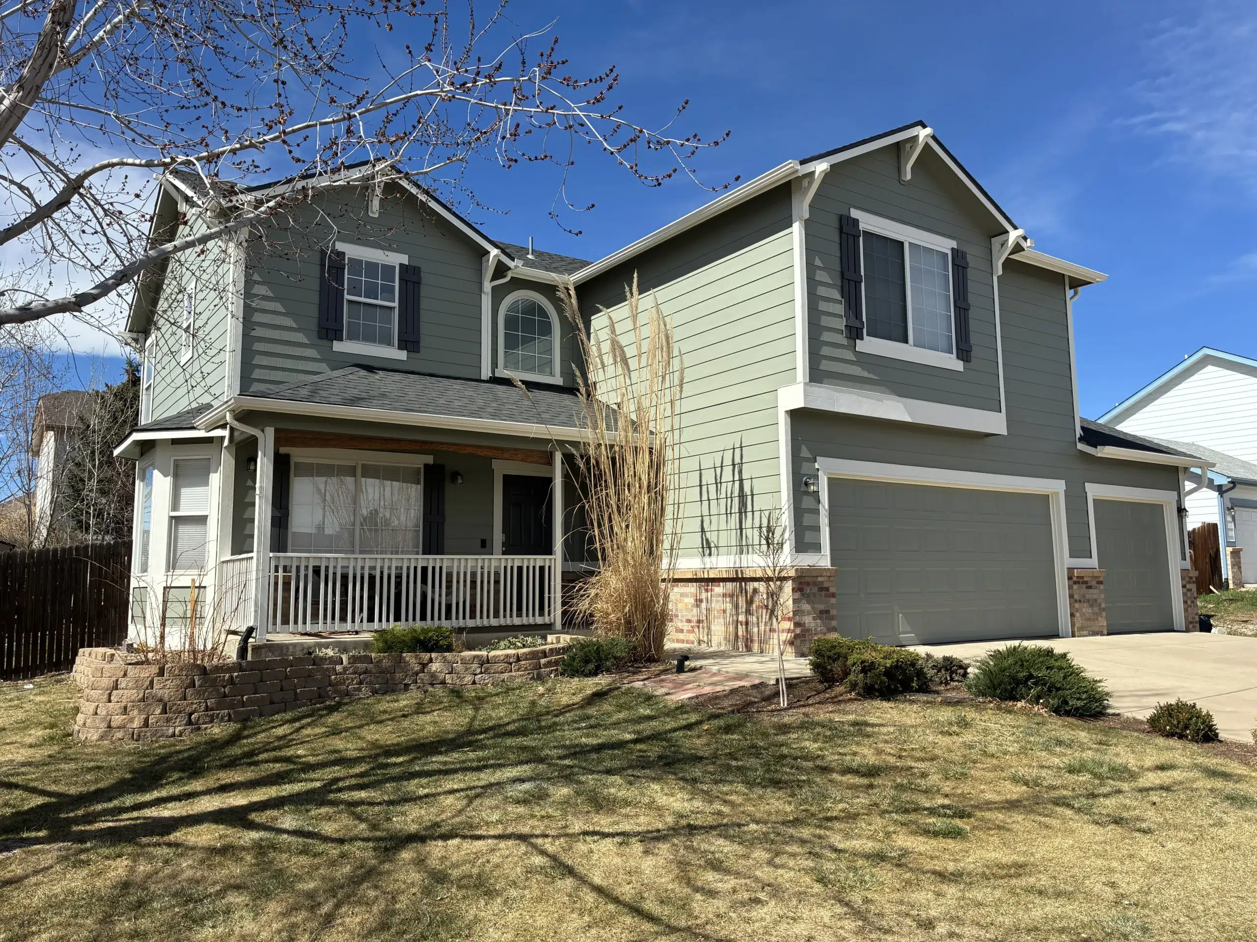 Completed exterior house painting project enhancing curb appeal Wide view of a beautifully painted residential home, featuring green siding, white trim, and an inviting front porch.