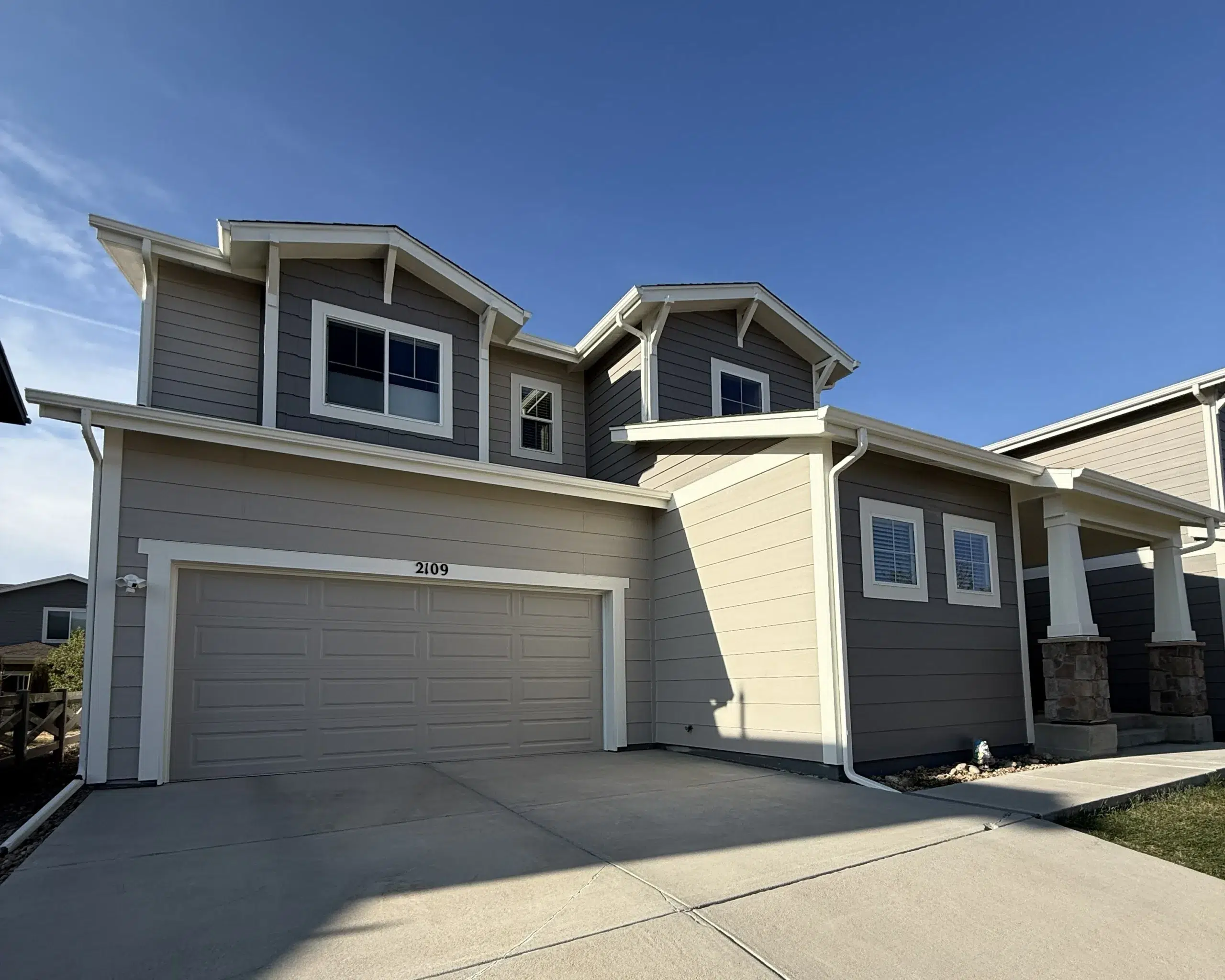 Modern Home Exterior Painting with Gray Siding and White Trim Modern two story house with light gray siding, darker gray accents, white trim, under a clear blue sky.