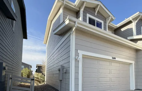 Residential Exterior Painting Project on a Modern Gray House Side view of a modern residential house with light gray siding, white trim, and a matching garage door.