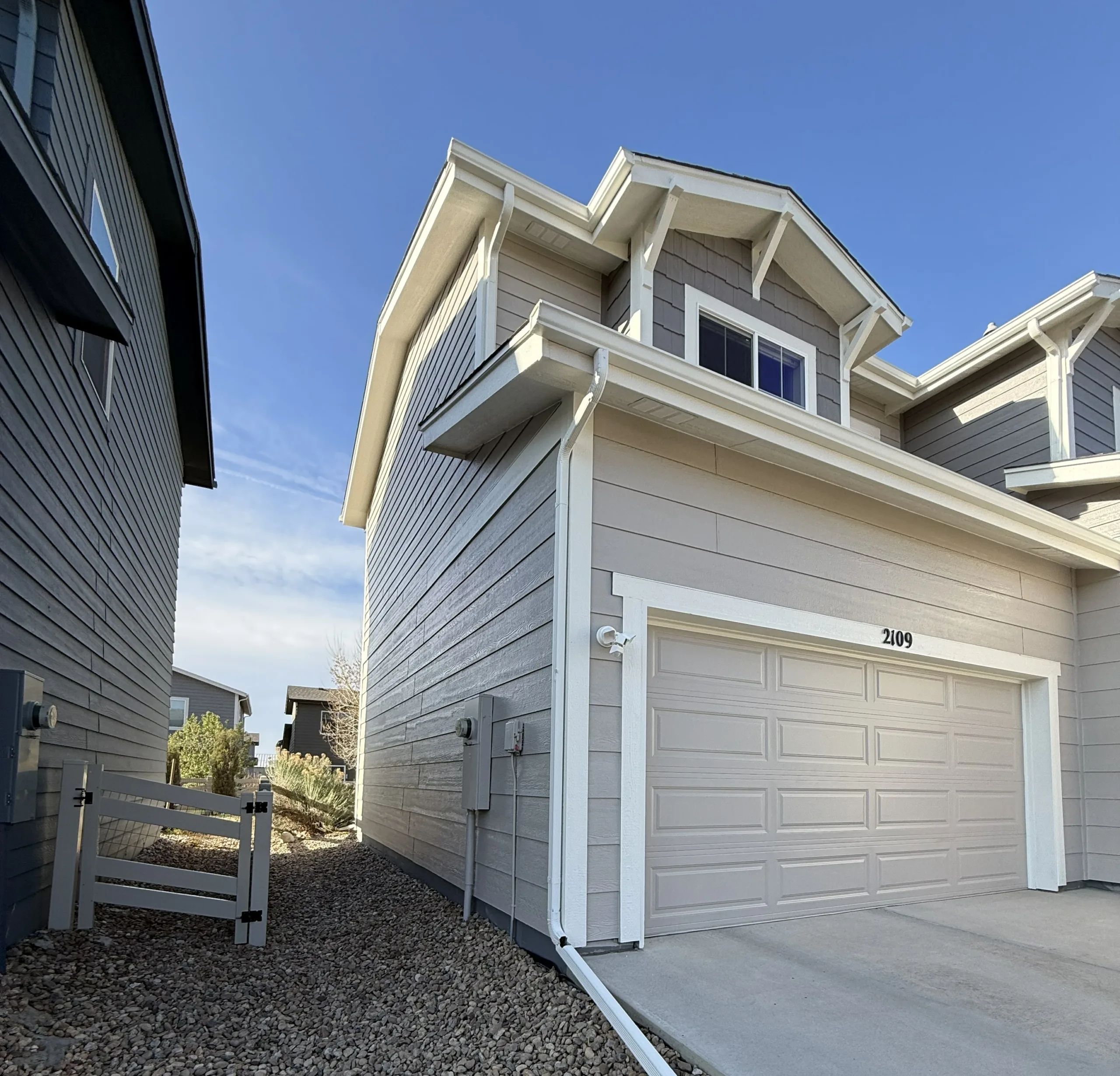 Residential Exterior Painting Project on a Modern Gray House Side view of a modern residential house with light gray siding, white trim, and a matching garage door.