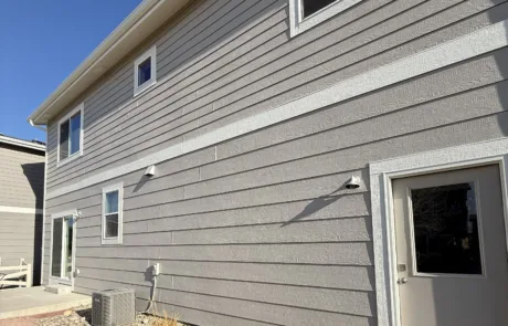 Professional Exterior Painting for Gray Siding and White Trim Back and side view of a modern house with gray painted siding, white window trim, and a back door.