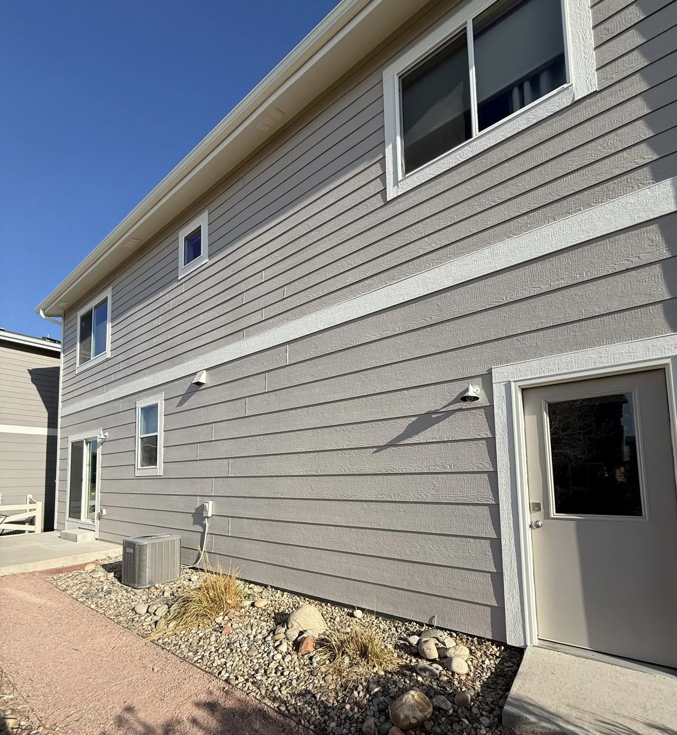 Professional Exterior Painting for Gray Siding and White Trim Back and side view of a modern house with gray painted siding, white window trim, and a back door.