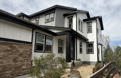 Modern Farmhouse Exterior Repaint – Two-Tone Siding with Stacked Stone Two-story modern farmhouse exterior with white and gray two-tone siding, black trim and stacked stone accent after repaint