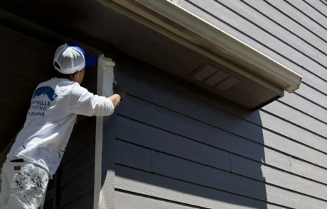 Professional Painter Applying Exterior House Trim Paint A professional painter meticulously applies a fresh coat of paint to the exterior trim of a gray residential house.