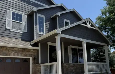 Professional Exterior House Painting Services for Curb Appeal Front view of a beautifully painted dark gray house with white trim and stone accents.