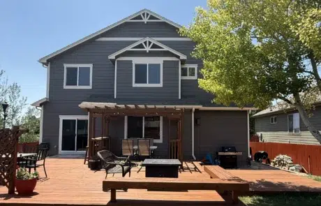Complete Back Exterior House Painting and Deck Staining Services Back of a dark gray house with a large stained wooden deck and pergola for outdoor living.
