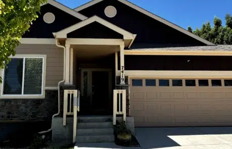 Black and Tan Residential Exterior Black gable-roof residential home with tan fiber cement siding, stone veneer base, cream entry columns, and tan garage doors