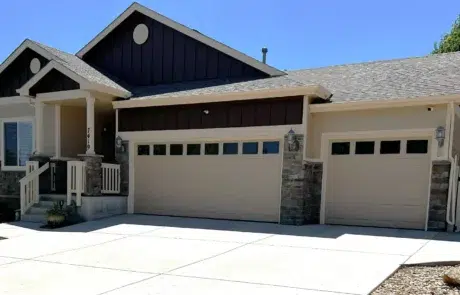Cream And Black Residential Exterior Cream-painted two-story residential home with black gable accents, stone veneer base, white-trimmed garage doors, and