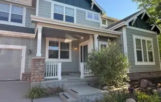 Gray fiber cement siding two-story home with dark gable accents, white-trimmed windows, stone veneer base, and white front