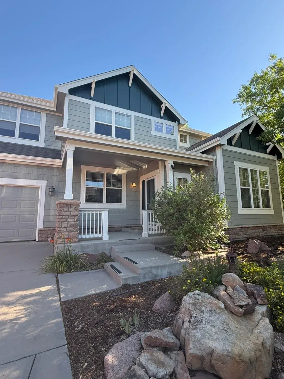 Gray And Green Exterior Residential Home Gray fiber cement siding two-story home with dark gable accents, white-trimmed windows, stone veneer base, and white front