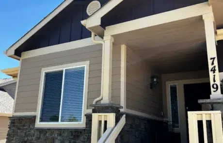 Tan And Navy Residential Exterior Tan fiber cement siding residential home with navy gable, cream trim columns, stone veneer base, and white-framed windows