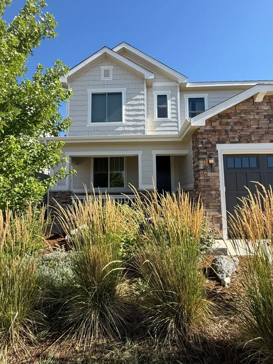 White Painted Two-Story Residential Home White painted two-story residential home with stone veneer base, dark garage doors, white trim, and gable roof