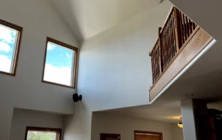 Bright white painted vaulted ceiling with wood-trimmed windows, dark ceiling fan, and wood railing in open residential