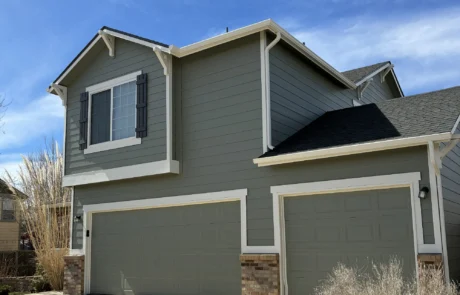 Sage Gray Two-Story Home Exterior Sage gray fiber cement siding two-story home with cream trim, dark shutters, black roof, stone veneer base, and white-framed