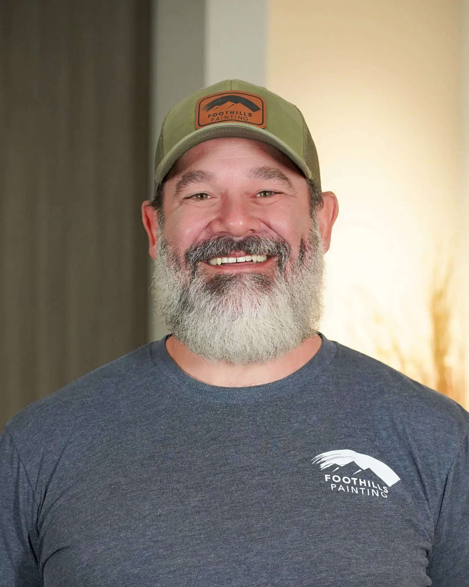 Foothills Painting Team Member Smiling man with gray beard wearing sage green Foothills Painting cap and dark gray branded t-shirt