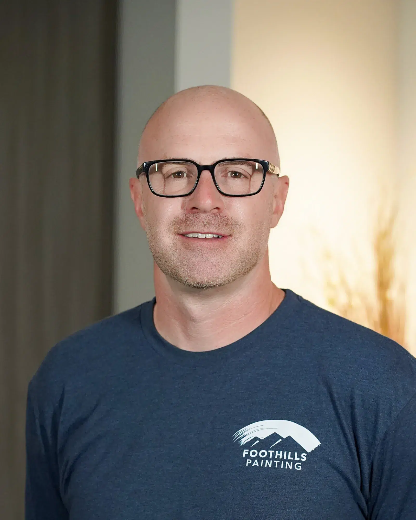 Foothills Painting Team Member Smiling man with light complexion wearing black-framed glasses and dark navy Foothills Painting branded t-shirt