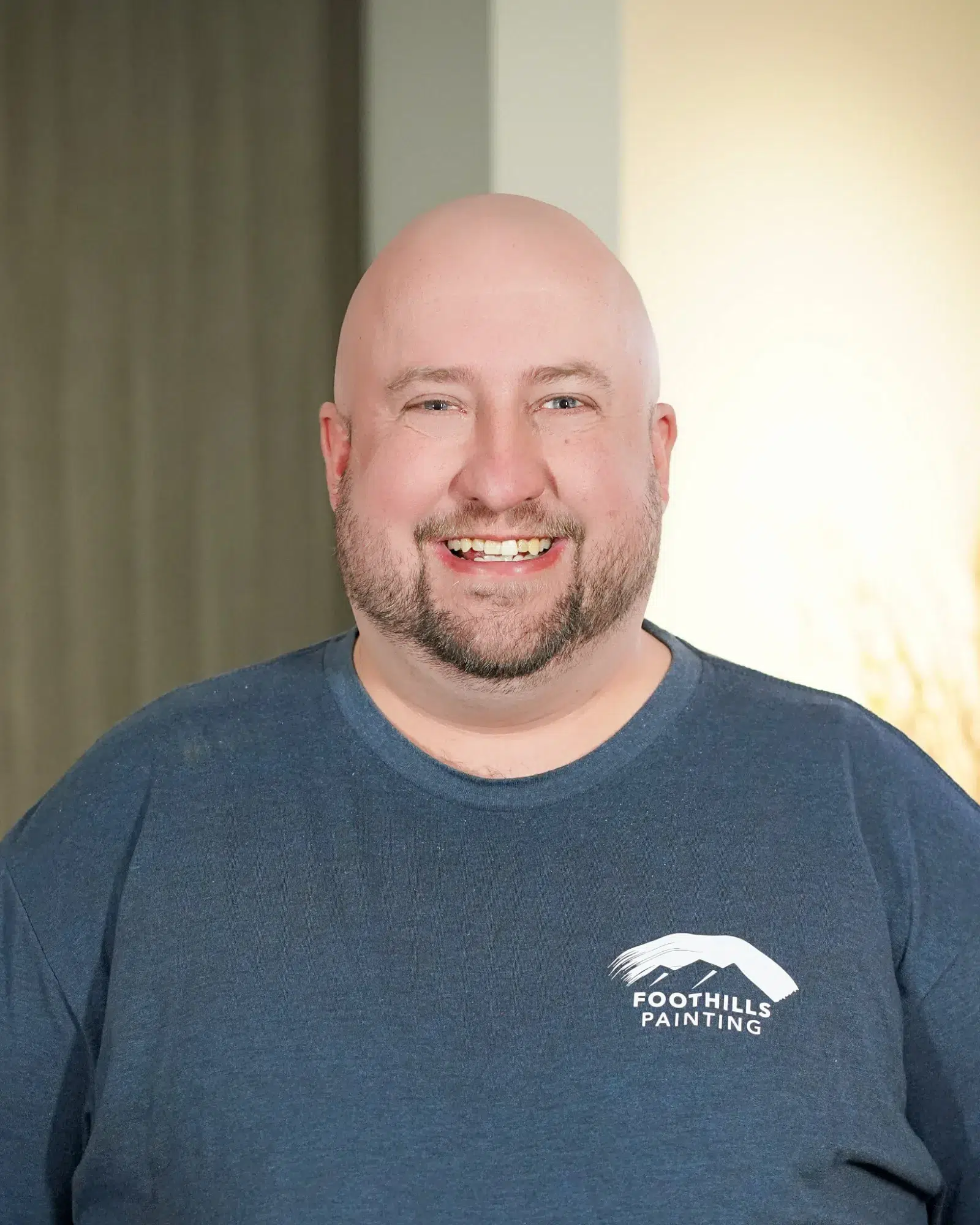 Foothills Painting Team Member Smiling man with light beard wearing dark navy Foothills Painting branded t-shirt against neutral wall backdrop